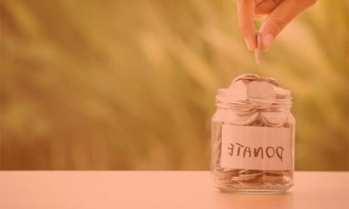 a hand putting money into a jar with the word donate written on it.