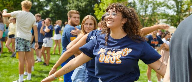 一个穿着“2026班”t恤的快乐年轻人在阳光明媚的日子里与其他参与者一起享受户外活动.